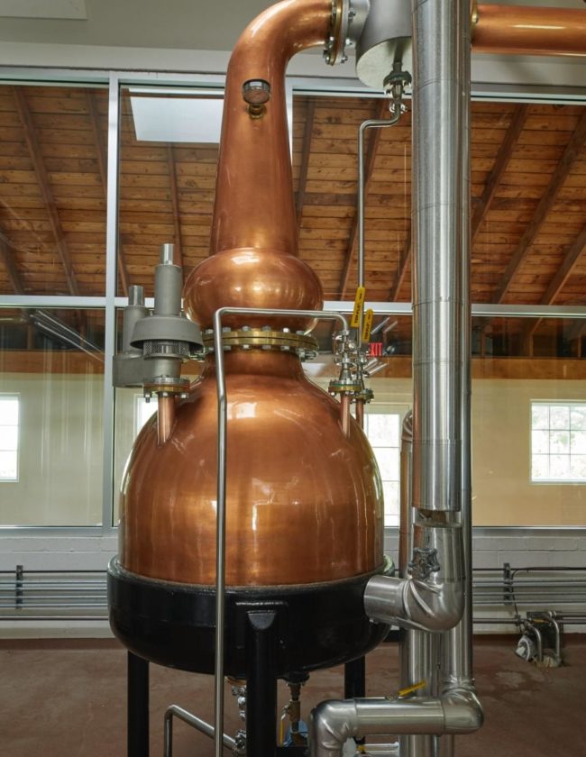 Large copper still in a room with large glass windows.