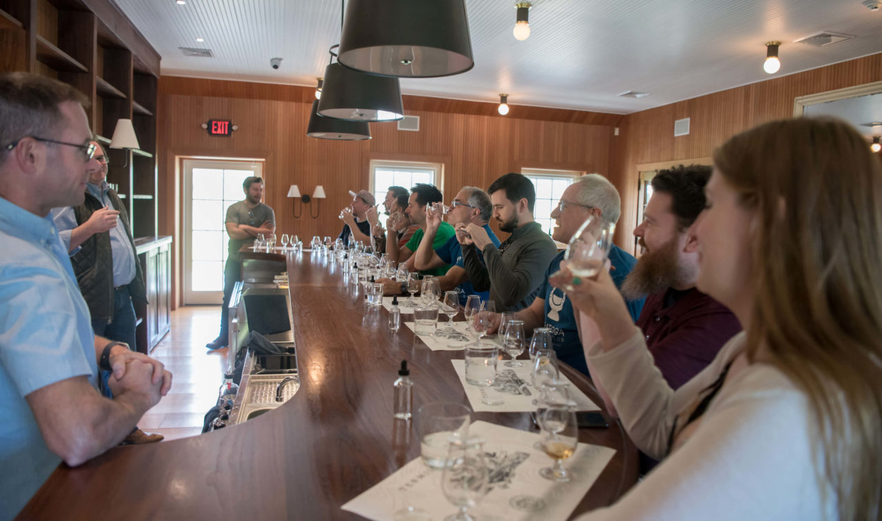 People seated at a long bar sipping from snifter glasses.