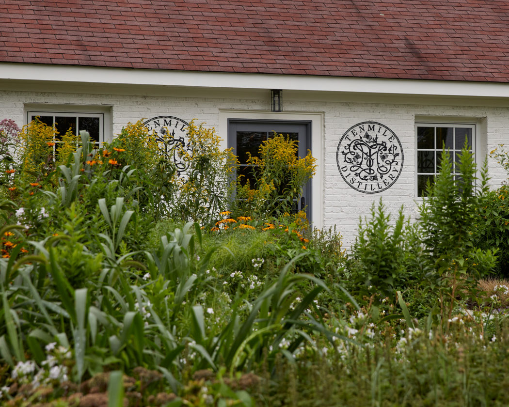 Tenmile Distillery Entrance White brick building surrounded by lush green landscaping.