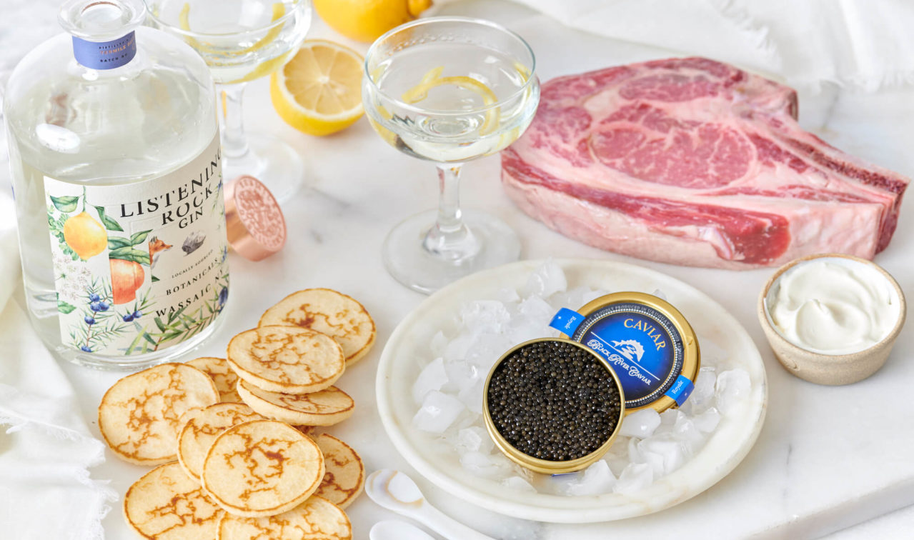 Large piece of steak on a table next to a tin of Black River Caviar.